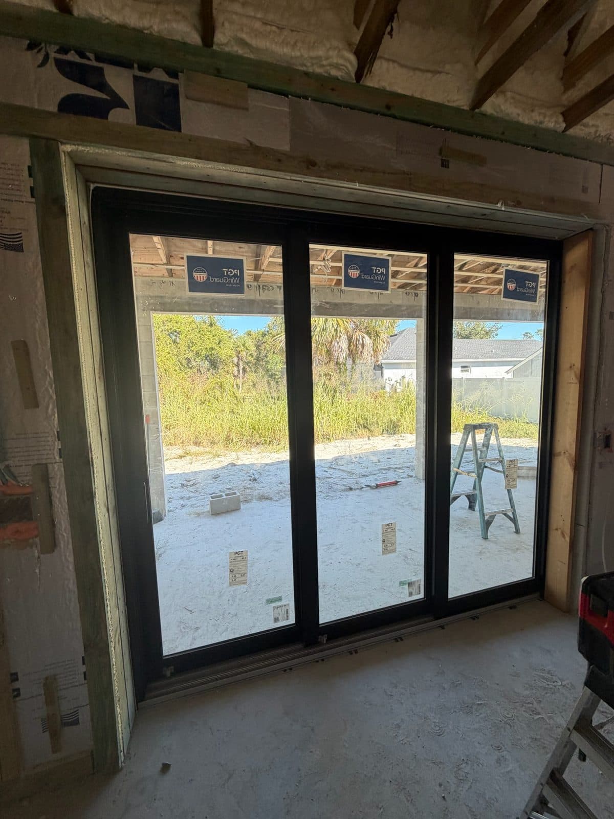 Black-frame PGT impact sliding glass door with labels installed in a block opening, North Port