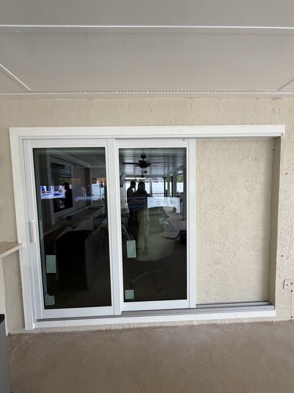 New white sliding glass door set in a stucco wall under a lanai ceiling
