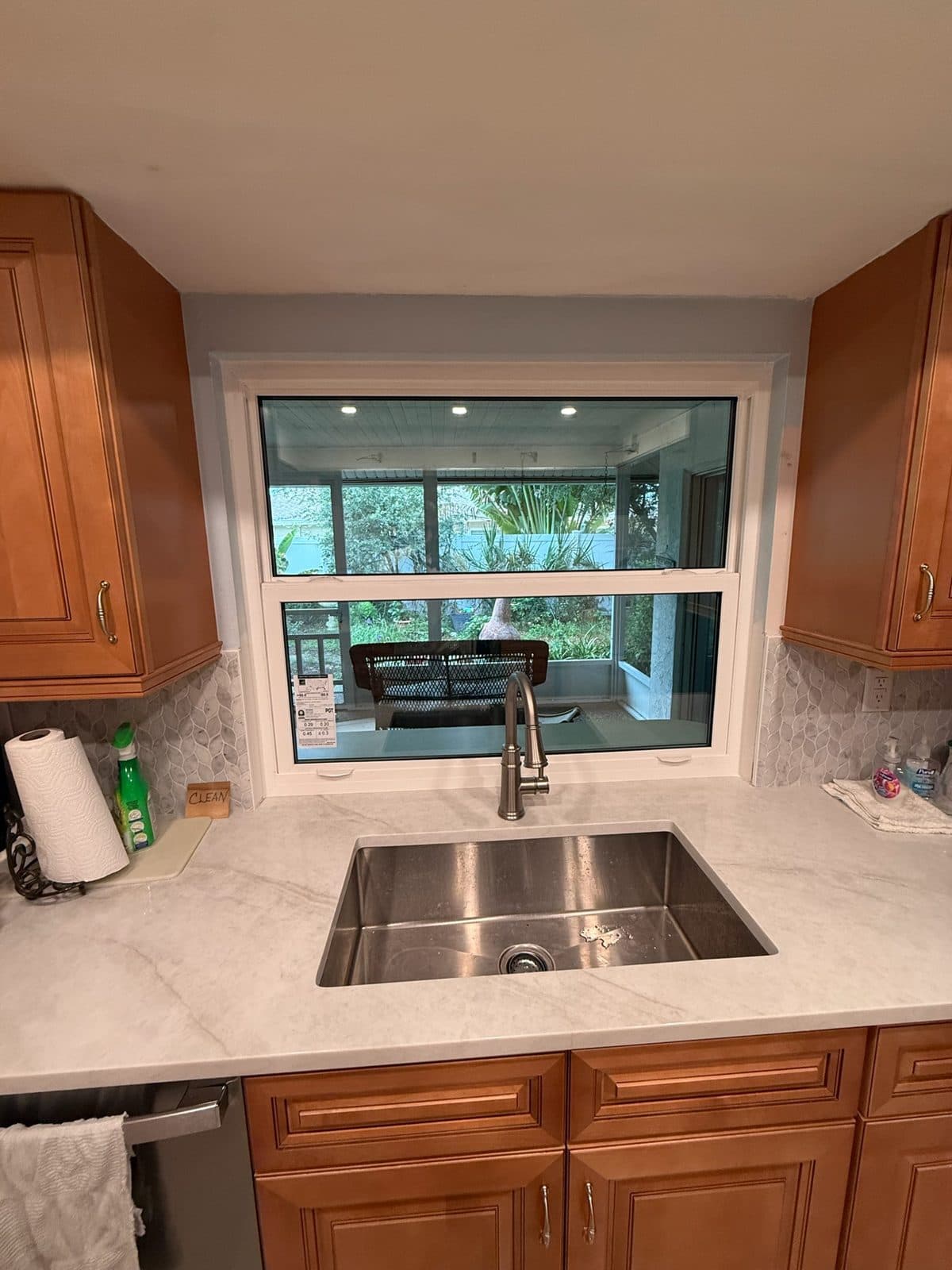 New white PGT single-hung window over an undermount stainless sink in a Sarasota kitchen with wood cabinets, white stone counter and marble mosaic backsplash