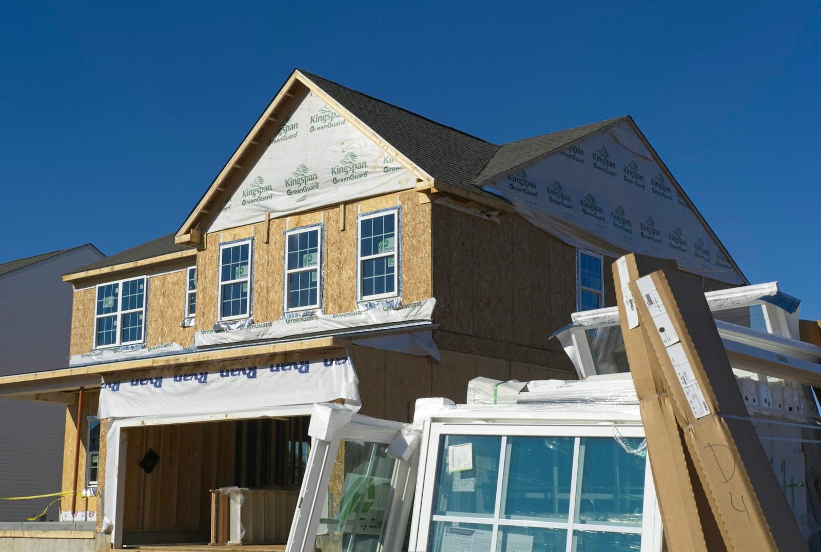 Home addition under construction with sheathed walls and new windows staged in front