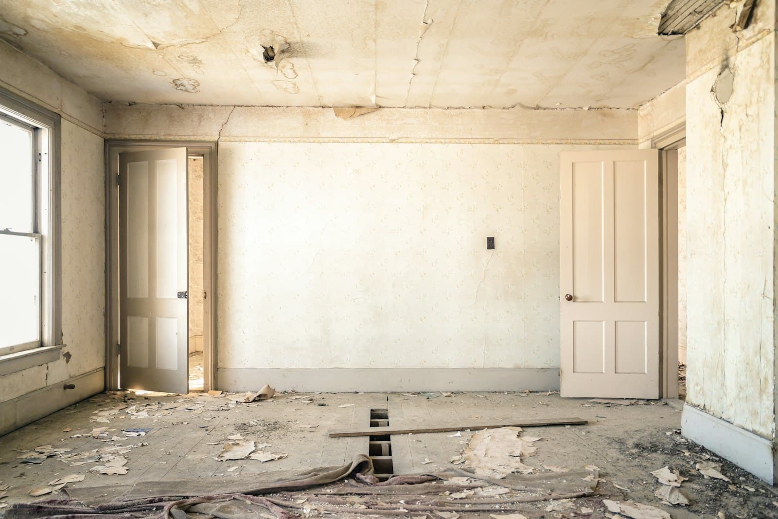Neglected room with peeling wallpaper and a damaged wood floor before a whole-home remodel